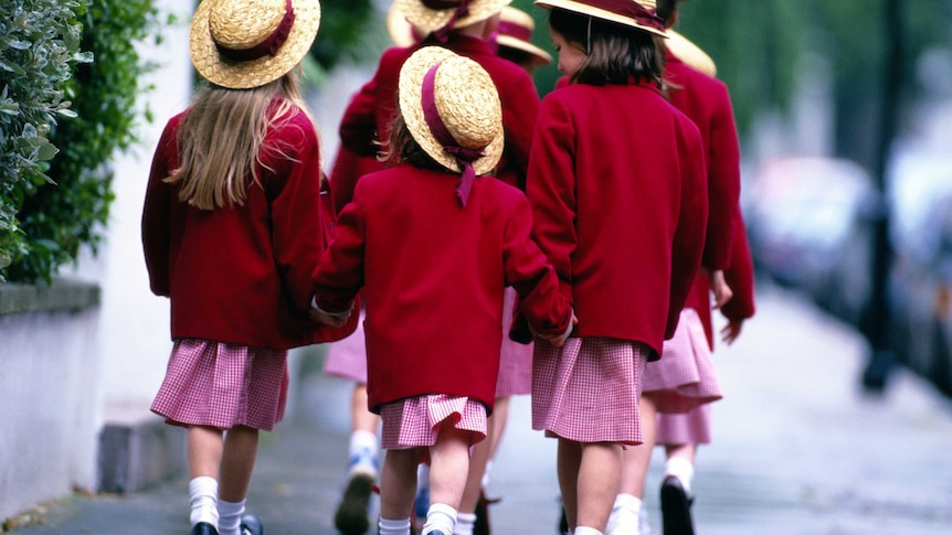 A group of young girls in red uniforms and straw hats walk to school.