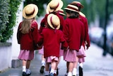 A group of young girls in red uniforms and straw hats walk to school.