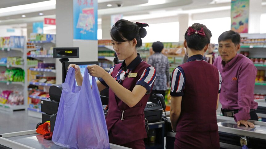 A woman working behind a checkout at a grocery store in North Korea packaging items in a purple bag