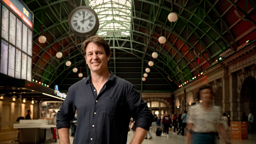 Craig Reucassel on a busy Central Station concourse, with commuters rushing past.