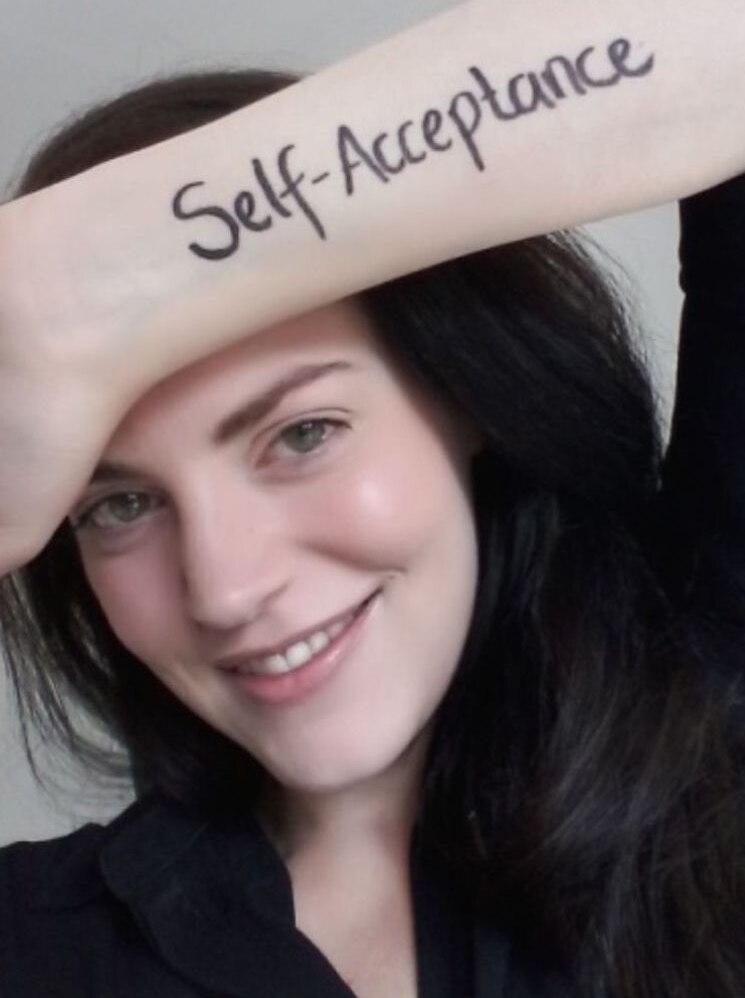 A woman smiling with 'self acceptance' written on her arm