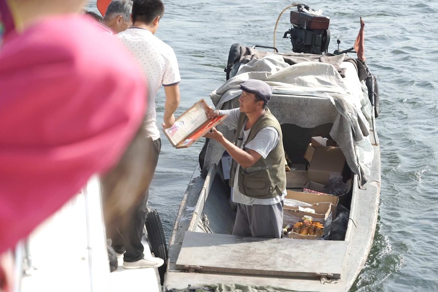 A man in a small boat shows off a souvenir to a larger boat full of tourists.