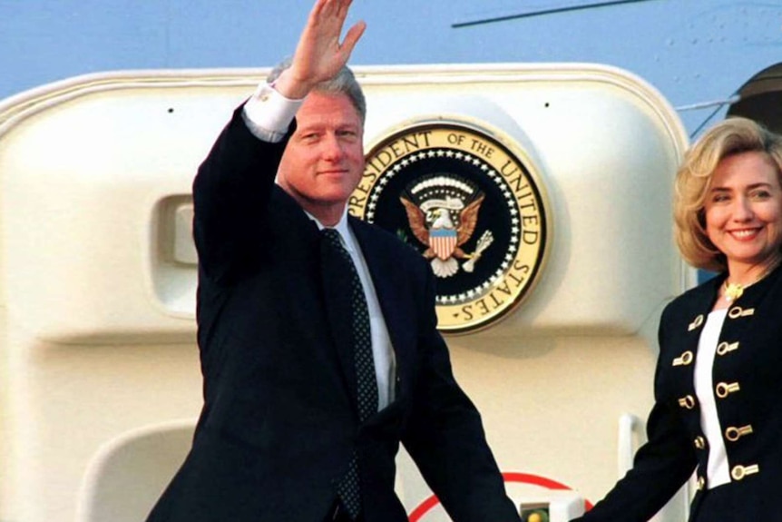 Bill Clinton has his hand above his head in a wave as he and Hillary board a presidential plane.
