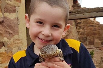 A young boy with short brown hair holds a Shingleback lizard close to his chest. Both are smiling.
