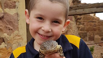 A young boy with short brown hair holds a Shingleback lizard close to his chest. Both are smiling.
