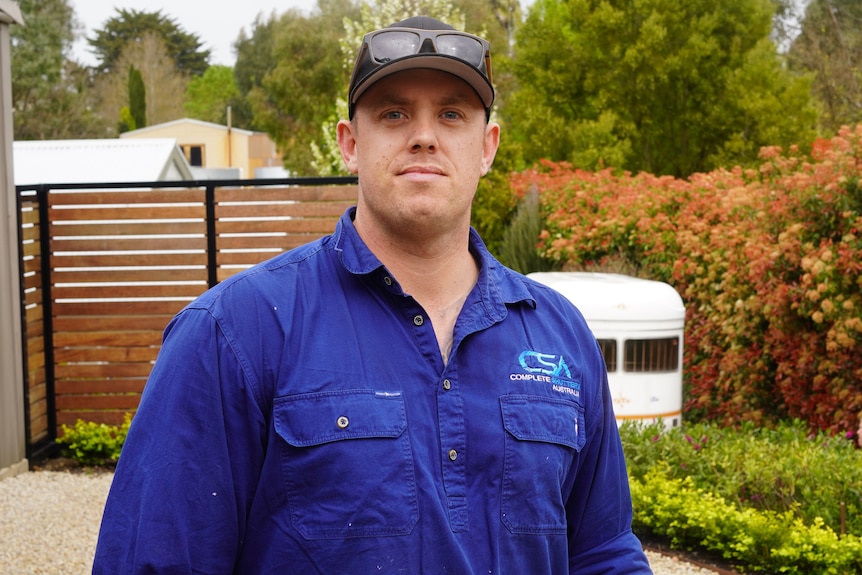 A man wearing a blue shirt and cap looks into the camera with a serious expression