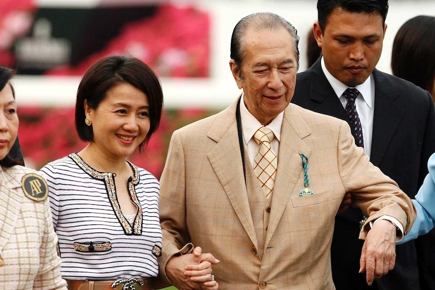 Stanley Ho is helped to walk by two women at a race track.