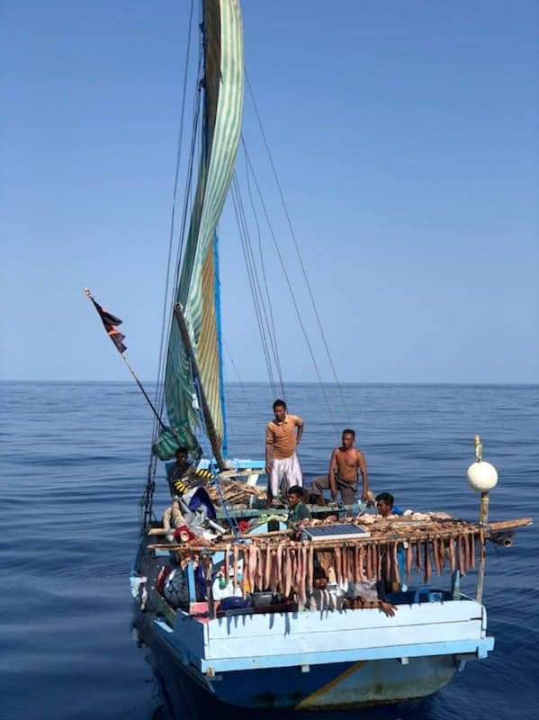 Indonesian fishermen stand on boat at sea.