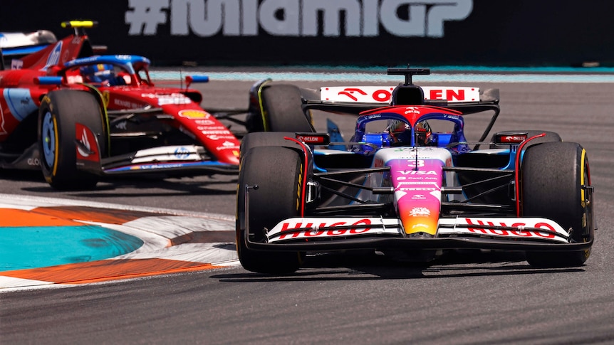 Two F1 cars, being driven on track in a race, fighting for position.