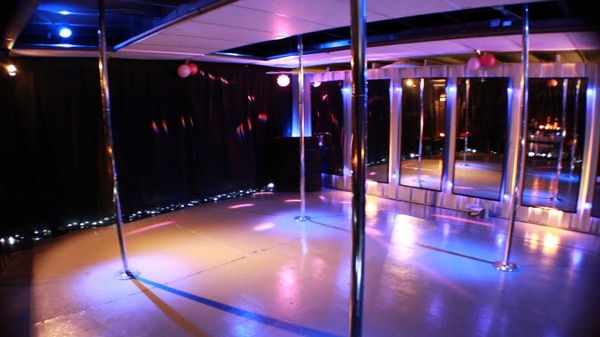 Four poles are visible in an otherwise empty pole dancing studio
