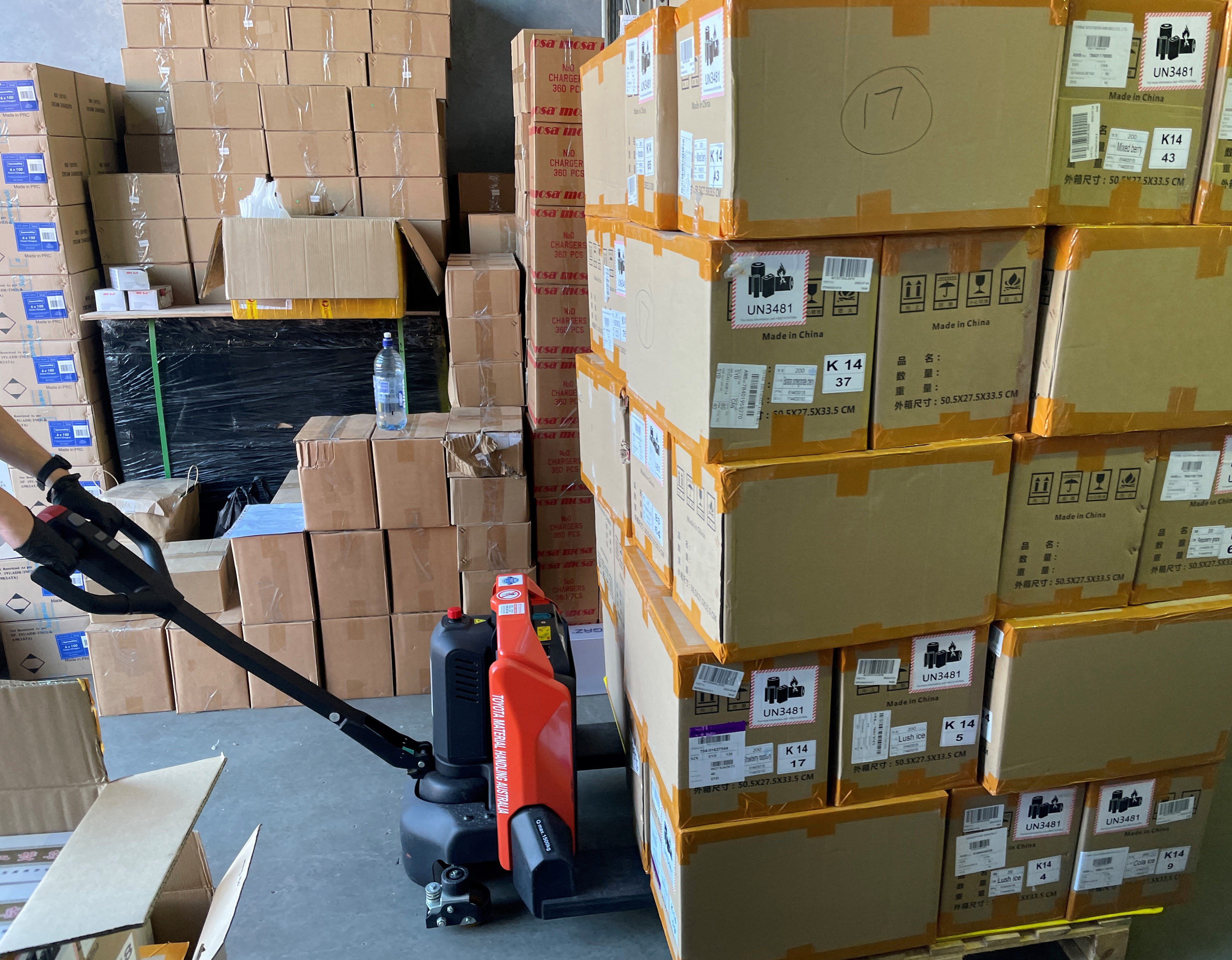 A close-up shot of a pallet of cardboard boxes being pulled by a red and black pallet jack.