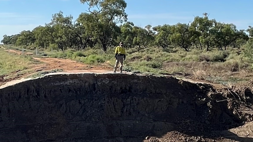 A man stands at the edge of a nine metre deep hole, caused by flooding in the Hay Shire in 2022. 