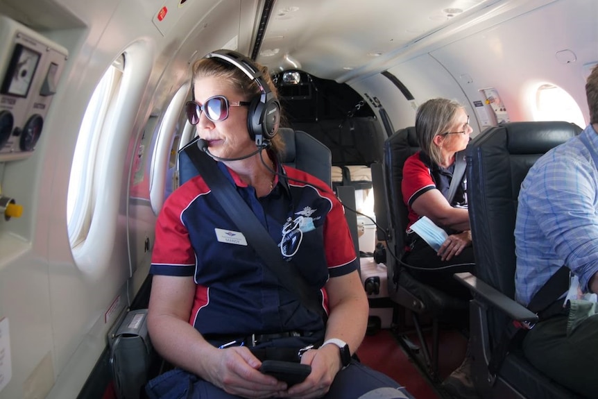 A nurse in uniform sits aboard a small aircraft and looks out window