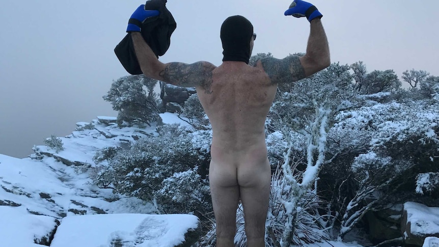 Man stands naked on top of mountain surrounded by snow
