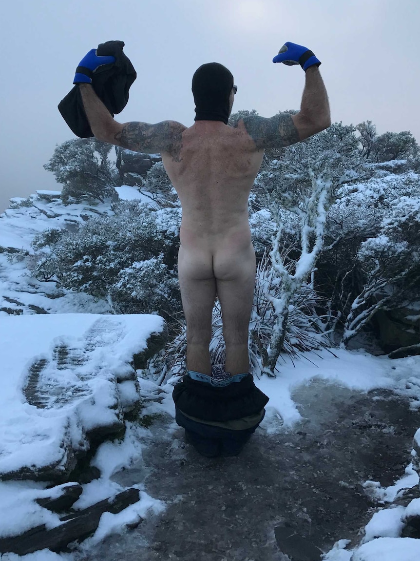 Man stands naked on top of mountain surrounded by snow