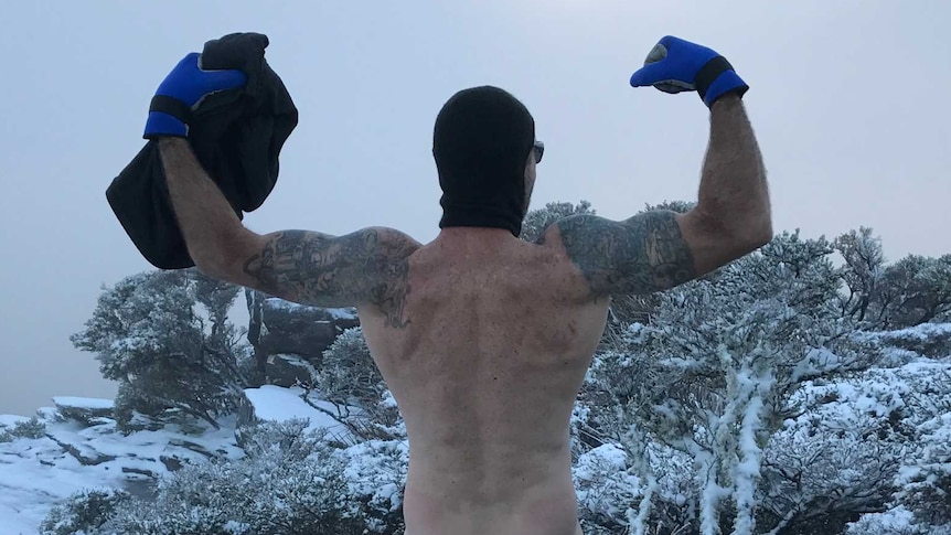 Man stands naked on top of mountain surrounded by snow
