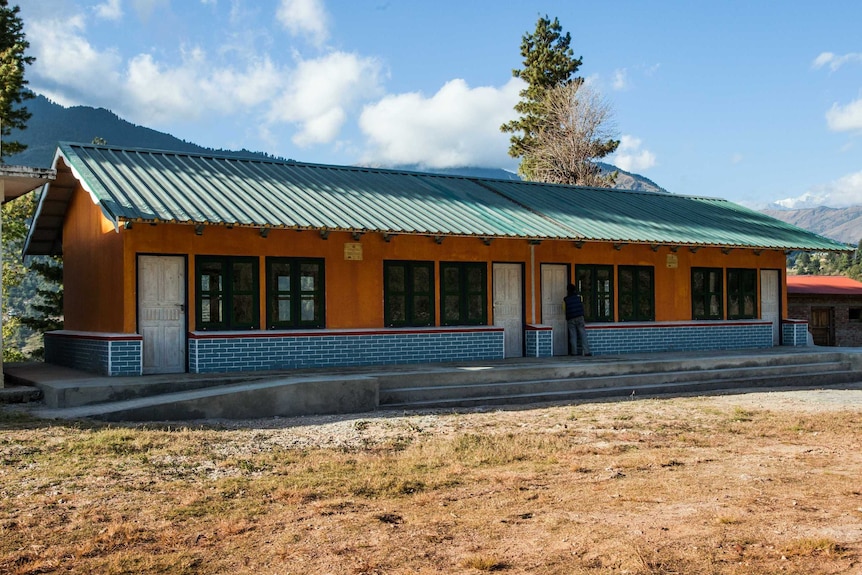 An earthquake  proof classroom in Nepal, with mountains and trees in the background.