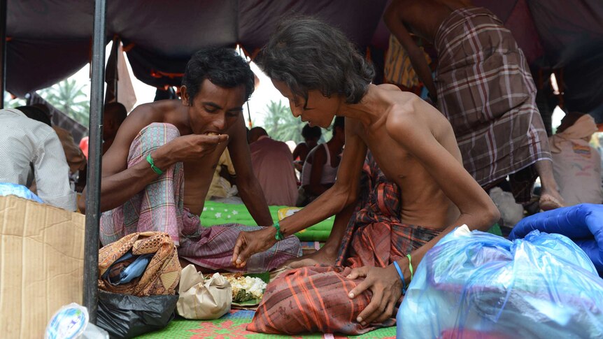 Rohingya men eat food at a confinement area for migrants