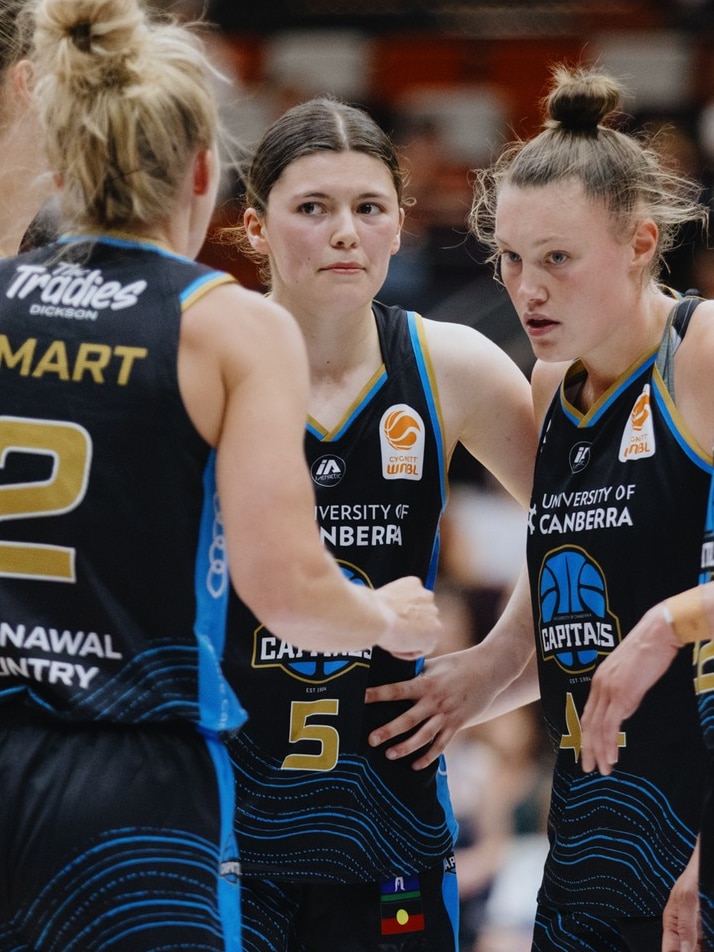 Women in blue basketball jersey's in a huddle.