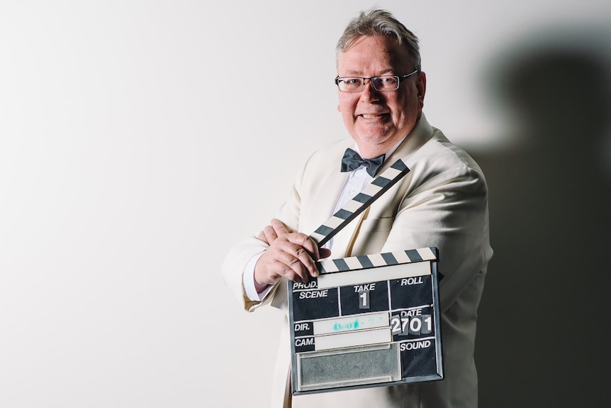 A man in a suit holds a film clapper board