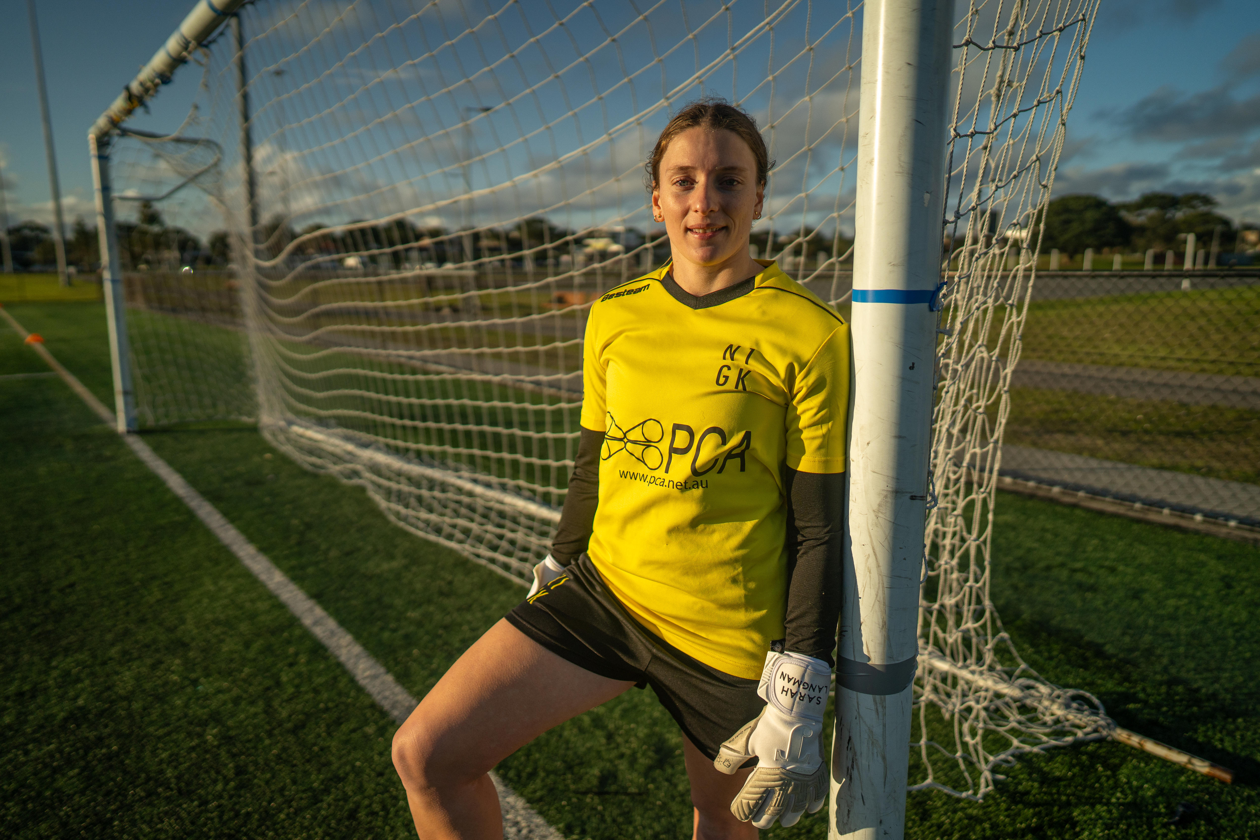 Female in yellow soccer jersey standing next to the goalposts. 