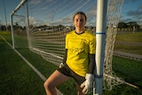 Female in yellow soccer jersey standing next to the goalposts. 