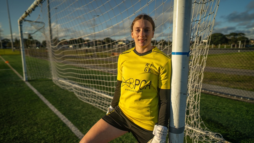 Female in yellow soccer jersey standing next to the goalposts. 