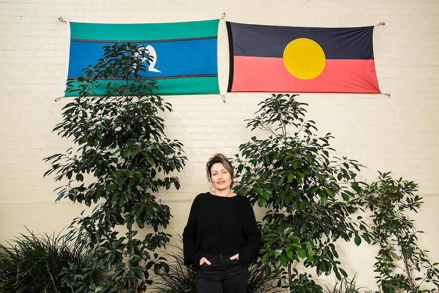 Woman stands in front of Aboriginal and Torres Strait Islander flag.