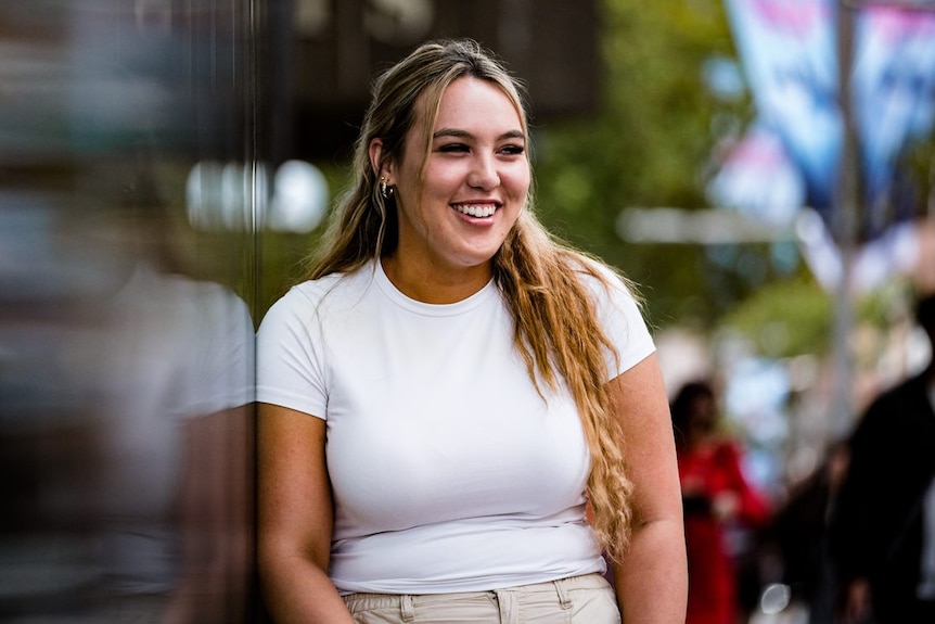 a young woman smiling as she leans up against a mirrored wall