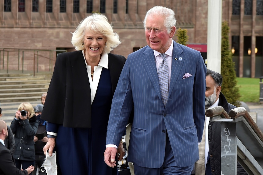 Camilla and Charles smile as they walk up the steps towards the camera.