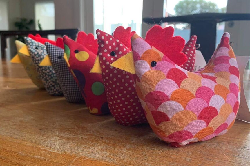 A line-up of several brightly-coloured fabric hens on a table.