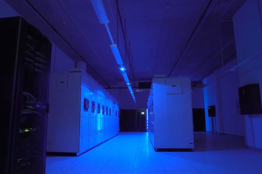 The inside of a darkened room with large cabinets in it illuminated by a dull blue light.