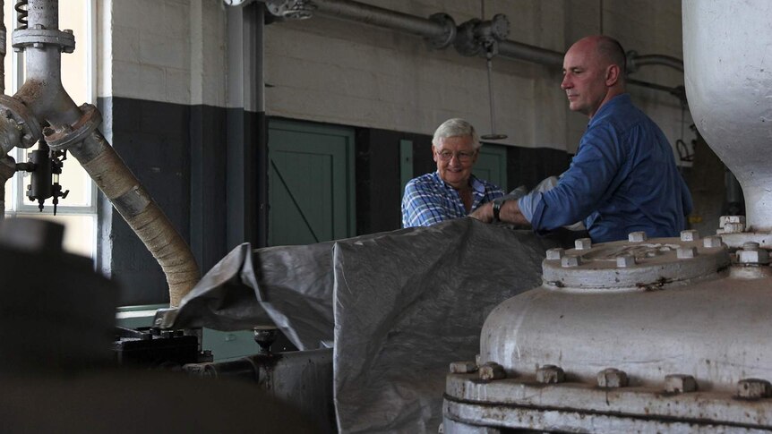 A photo of Trevor Horman and Michael Wells pulling the tarp off equipment in the steam house.