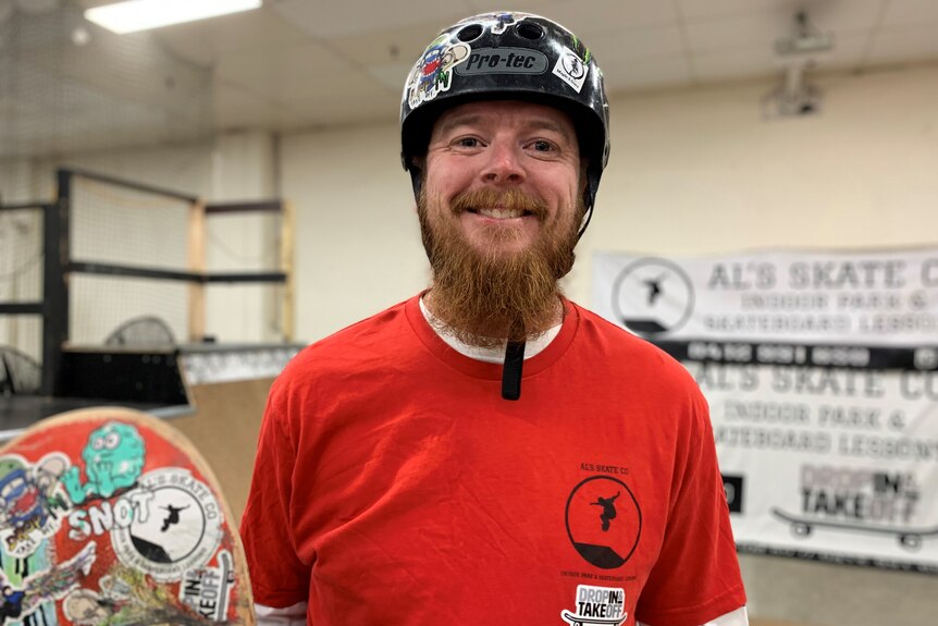 Al Taylor smiles at camera  and wears a skateboard helmet in an indoor skate park