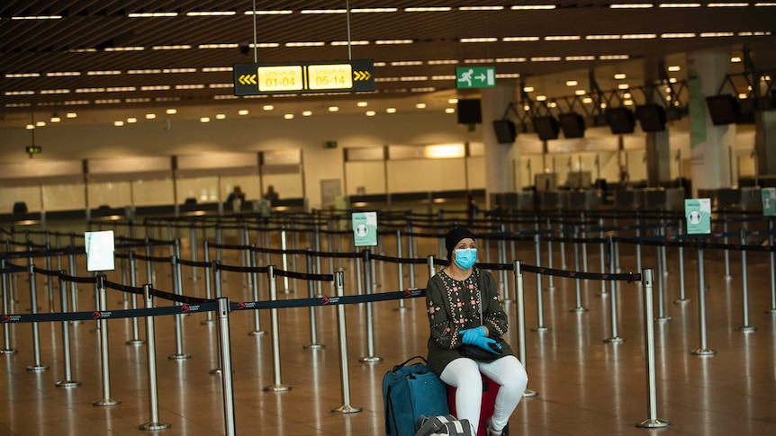 A passenger, wearing a face mask to protect against the spread of coronavirus, sits at the almost empty departures hall.