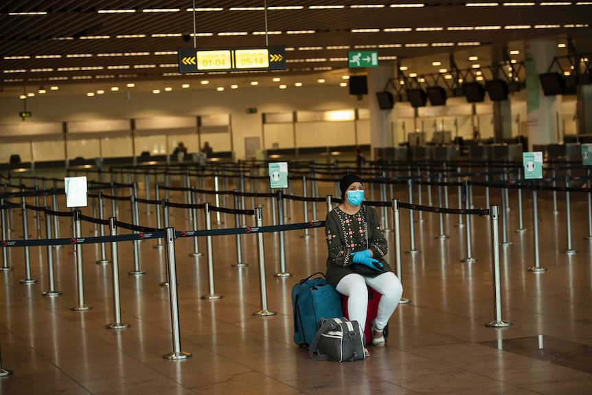 A passenger, wearing a face mask to protect against the spread of coronavirus, sits at the almost empty departures hall.