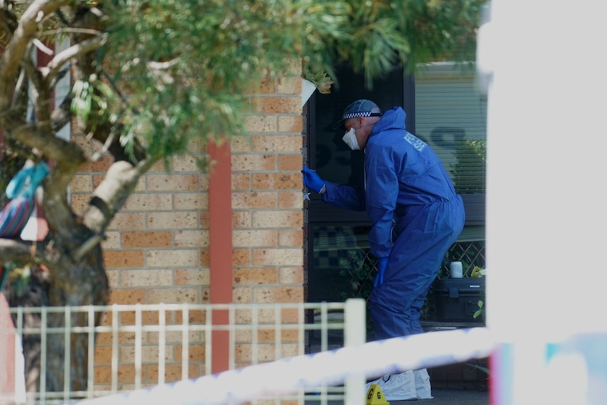 A police forensic officer dusts for fingerprints at the front door to a house.