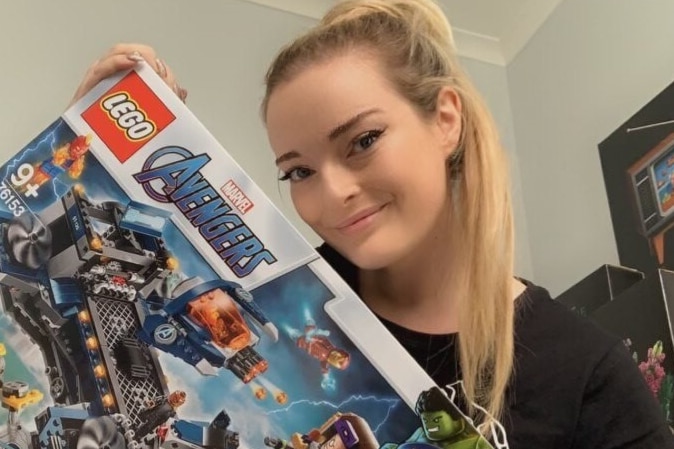 A woman with a blonde ponytail holds a box of Lego.