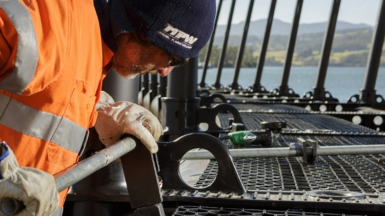 Man working on a plastic salmon enclosure on a waterway.