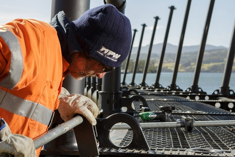 Man working on a plastic salmon enclosure on a waterway.