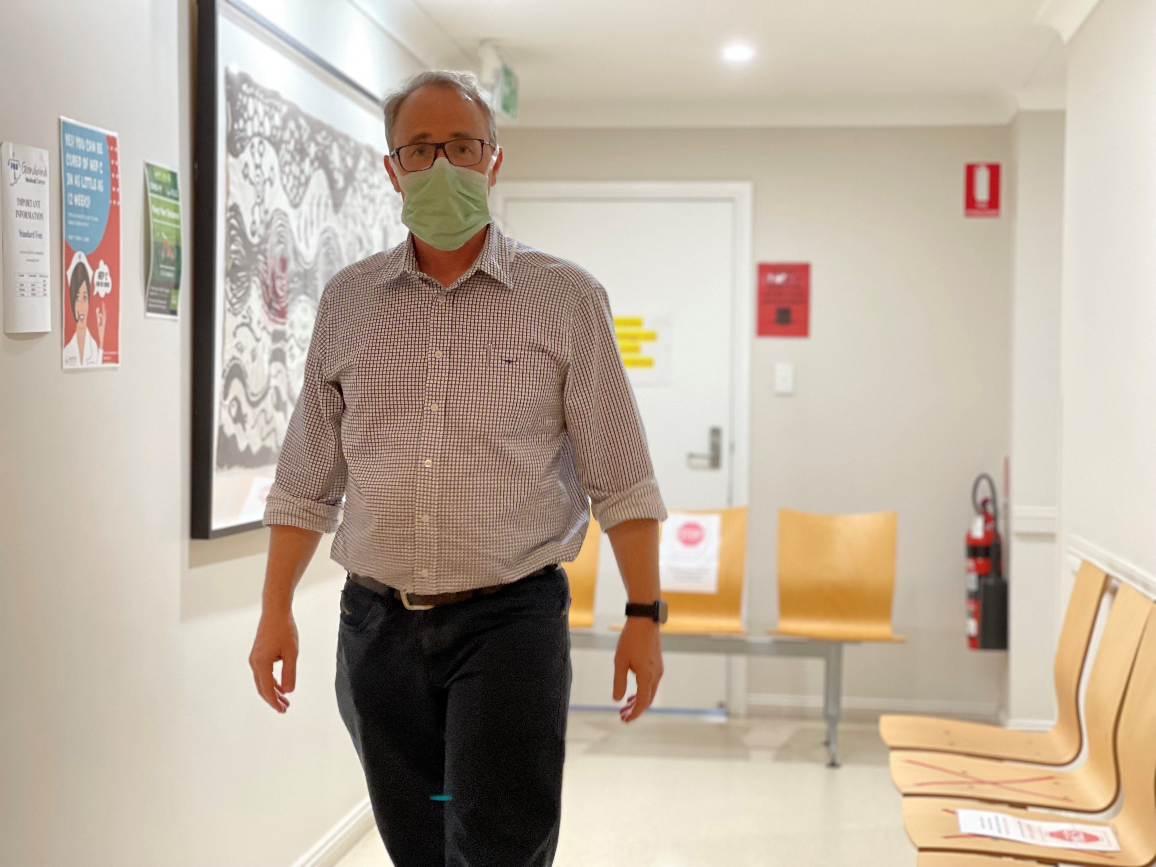 A man standing in a corridor, wearing a mask