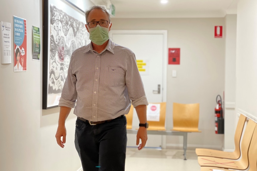 A man standing in a corridor, wearing a mask