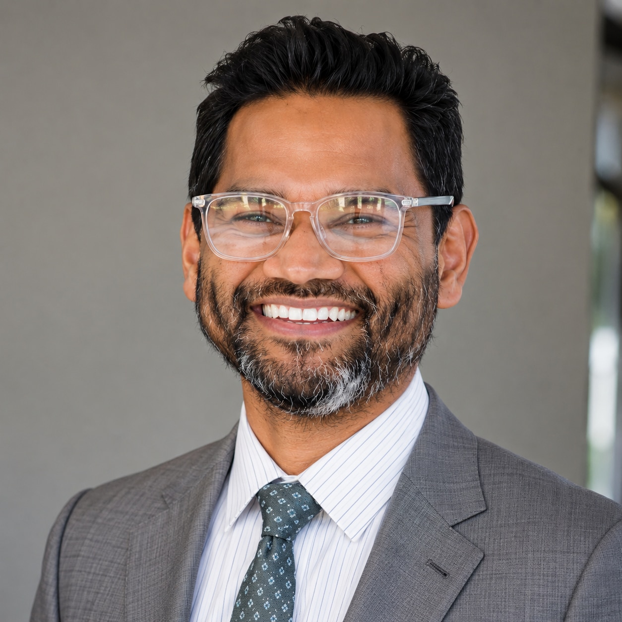 A man in a suit and glasses smiling into the camera.