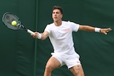 A male tennis player wearing white hits a ball with his racquet during a match