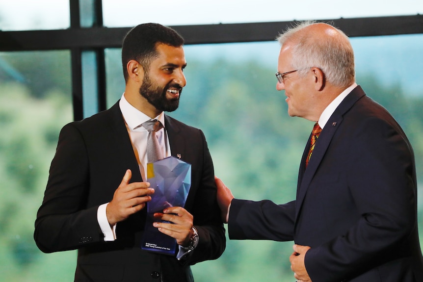 A man, holding an award, is congratulated by Scott Morrison.