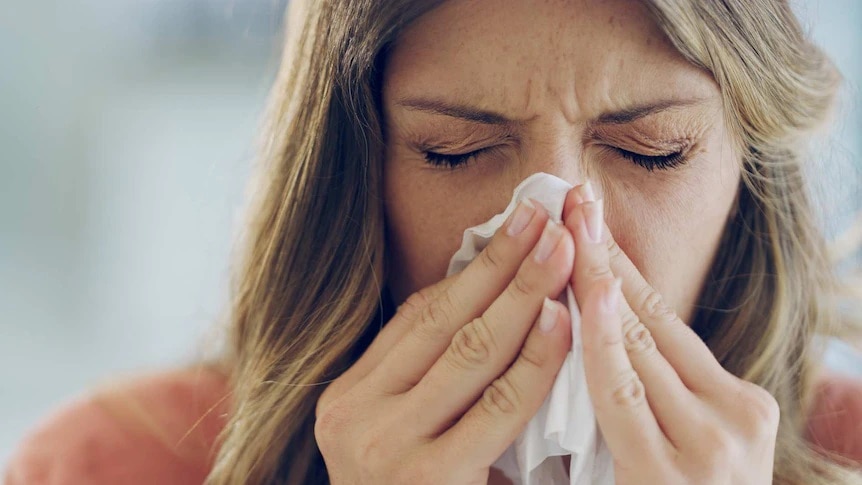 A woman sneezes into a tissue