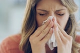 A woman sneezes into a tissue