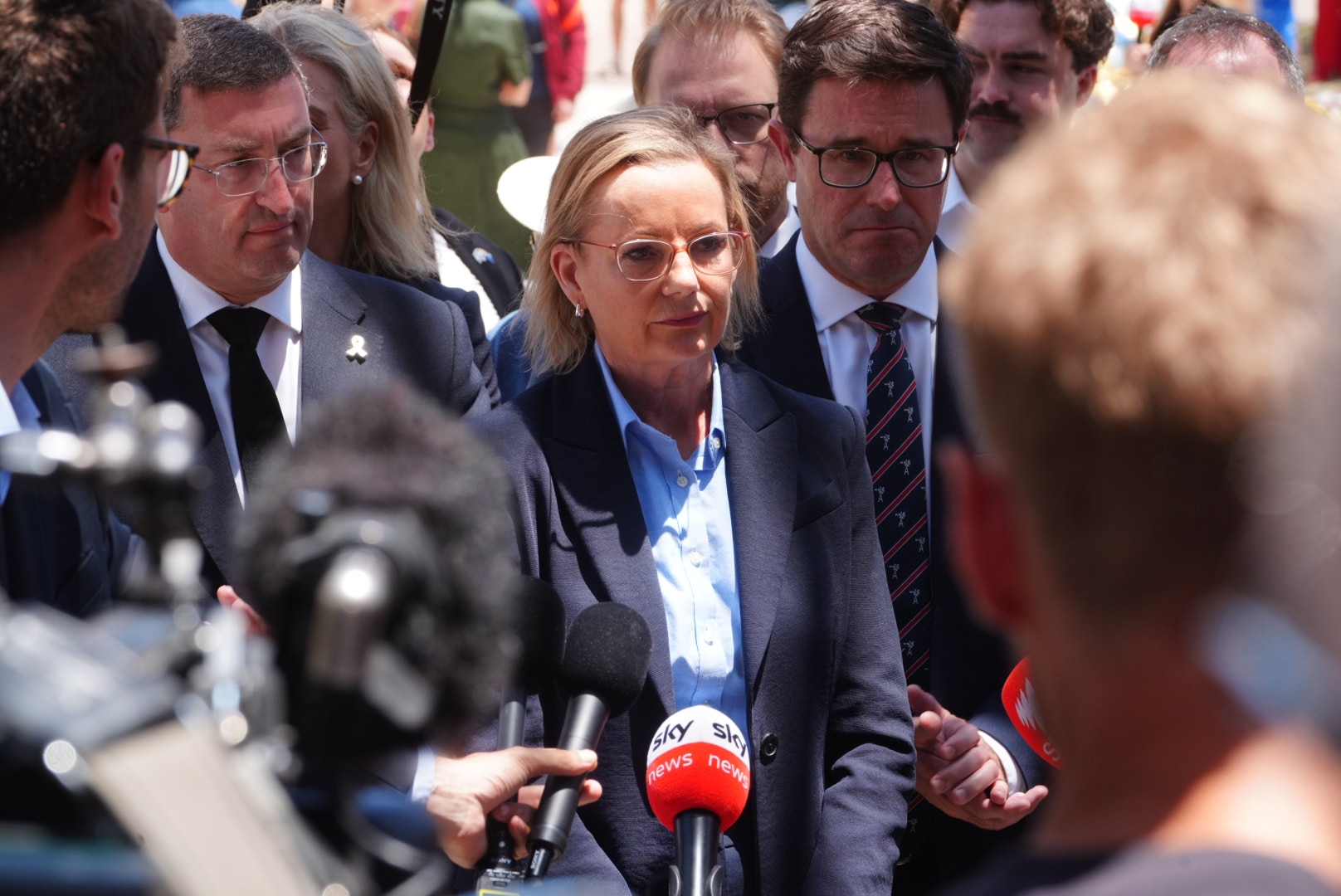 Sussan Ley presenta un paquete mediático y luce seria. Detrás están Julian Leeser y David Littleproud.