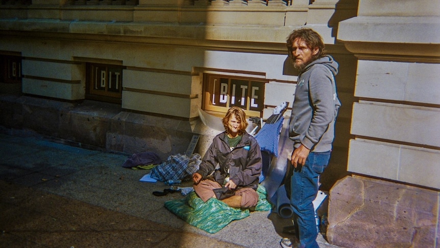 Two homeless men sitting on the street.