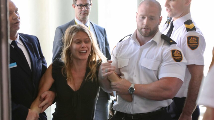 A protester cries as she is escorted out of Parliament House by a group of security guards.